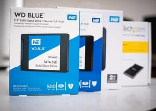 Boîtes de disques SSD 2,5 pouces neufs alignées sur un plan de travail, à côté d’un boîtier de disque externe.