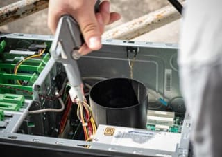 Une main intervient à la pince sur le câblage d’un ordinateur ouvert, près de son bloc d’alimentation.