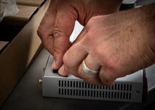 Deux mains mettent en marche un petit boîtier réseau posé sur un plan de travail.