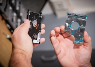 Deux mains présentent un disque dur 2,5 pouces monté et le circuit imprimé d’un second disque démonté.