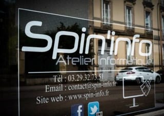 Vitrine gravée au nom de l’atelier, avec le téléphone, l’adresse électronique et l’adresse du site, et le reflet de la rue.