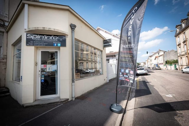 La boutique vue de la rue, enseigne et oriflamme « Ouvert » devant la vitrine.