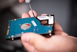 Un disque dur 2,5 pouces ouvert au tournevis, tenu à la main.