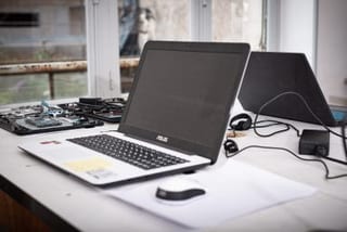 Ordinateur portable ouvert sur un plan de travail, à côté d’un appareil en cours de démontage.